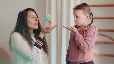 Junge Frau spielt mit einem Kind, sie lassen selbstgebastelte Schmetterlinge fliegen