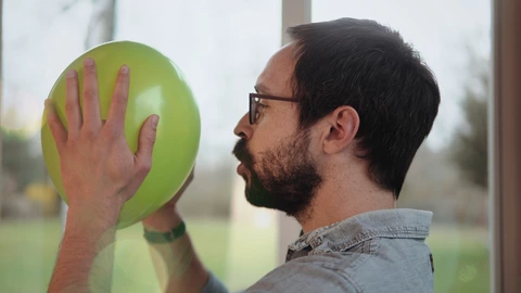 Mann hält einen Luftballon in der Hand und pustet gegen ihn
